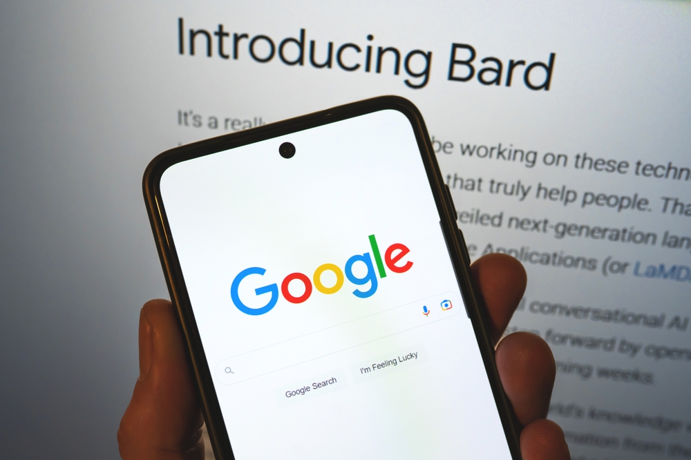 a person holding a cell phone with the google logo on it and Bard behind his hand